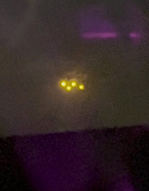Ночное фото: кластер желтых огней UFO над горизонтом, пятна света в небе и фиолетовые блики